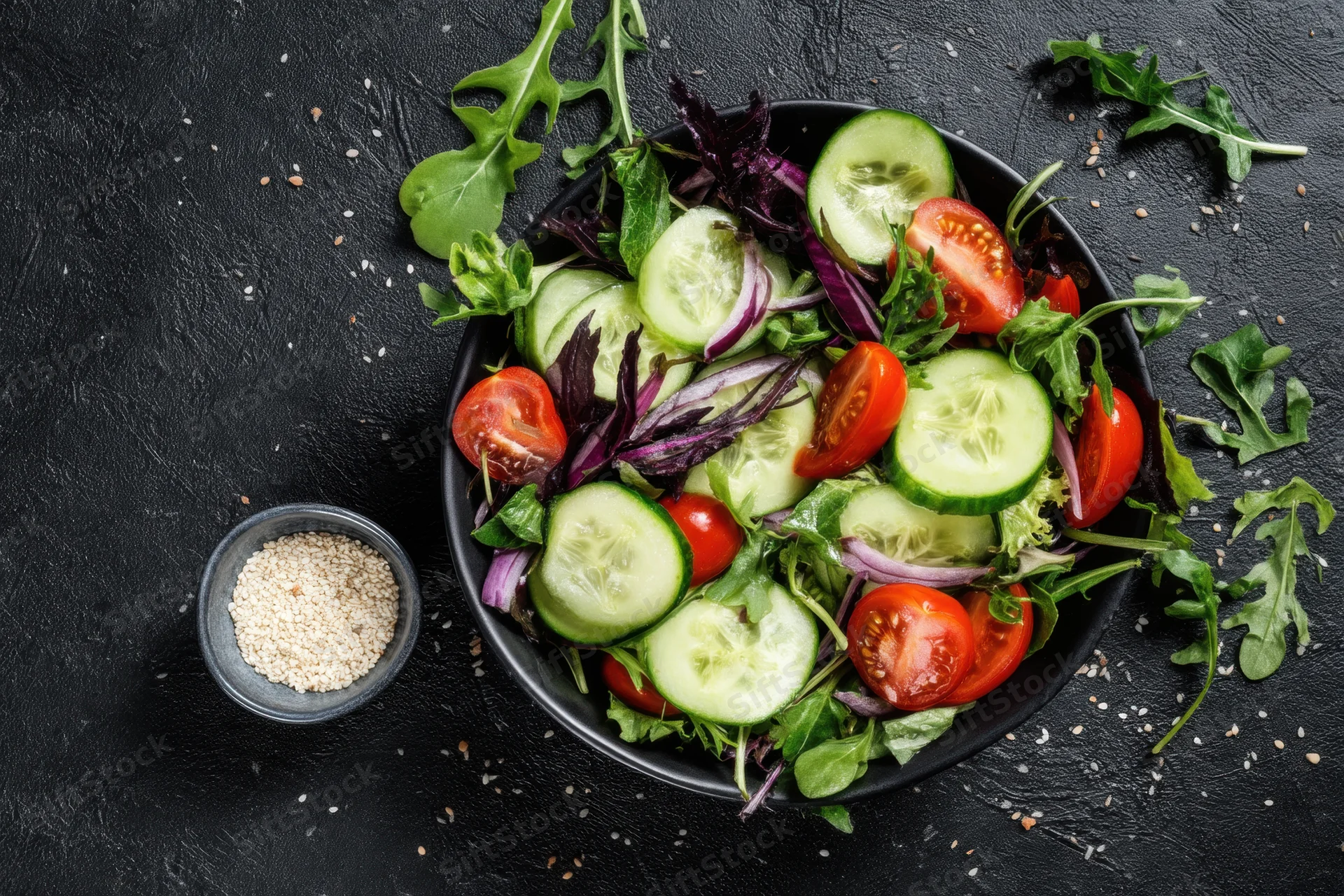 Fresh salad with cucumber slices cherry tomatoes and arugula in a black bowl on dark textured surface