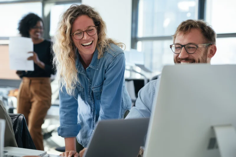 Woman laughing with colleague at computer in bright office space