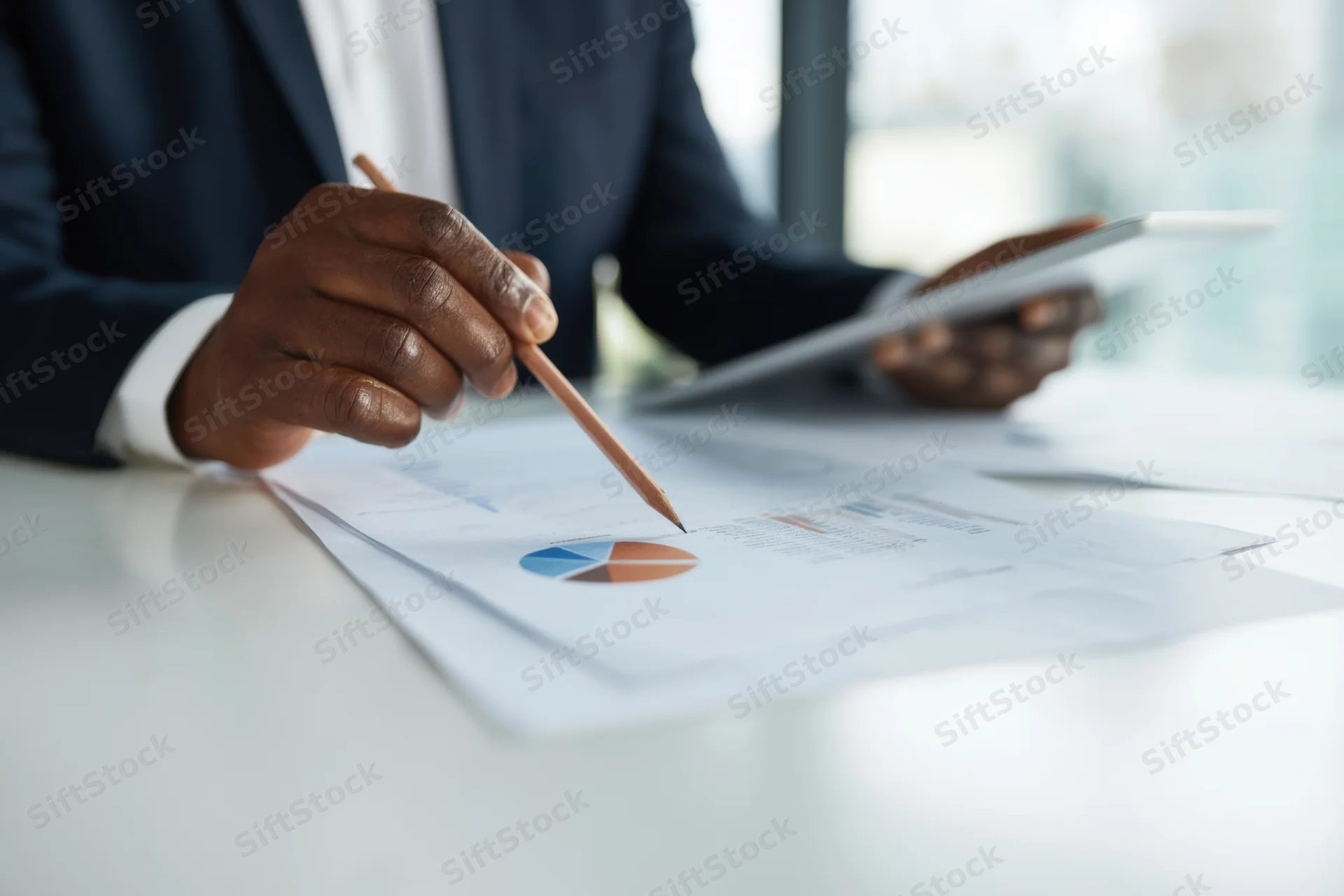 Man in dark suit pointing at pie chart on document with pencil at office desk