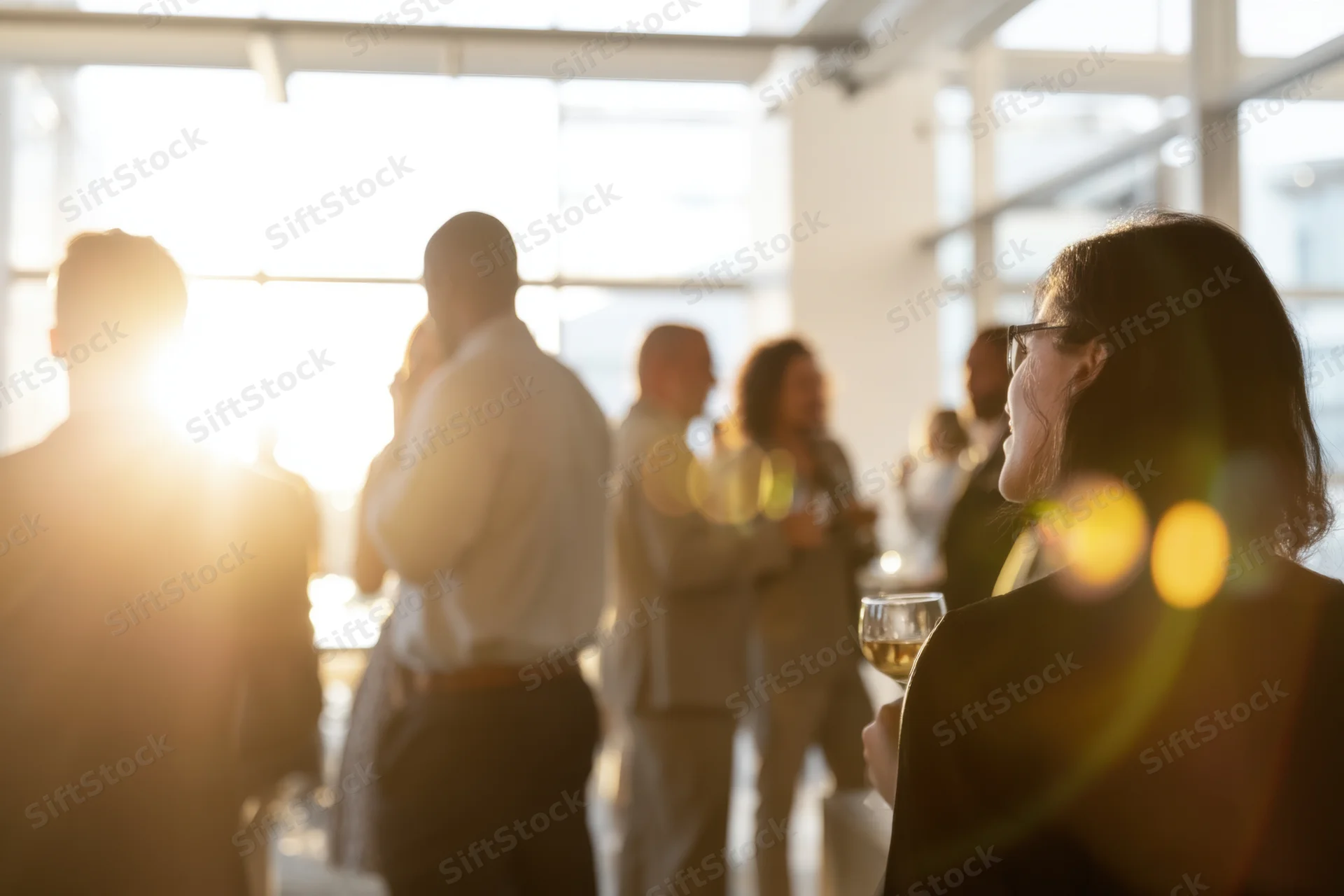 Woman in profile holding wine glass at office social event with colleagues in background