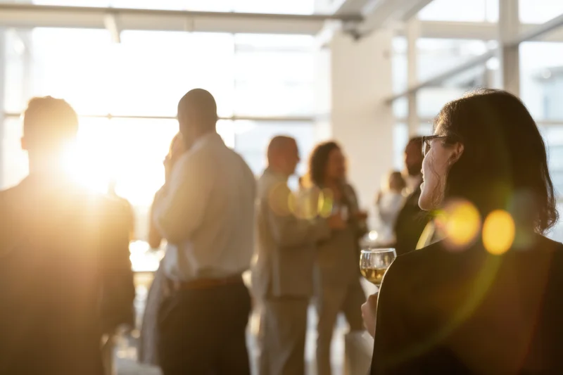 Woman in profile holding wine glass at office social event with colleagues in background