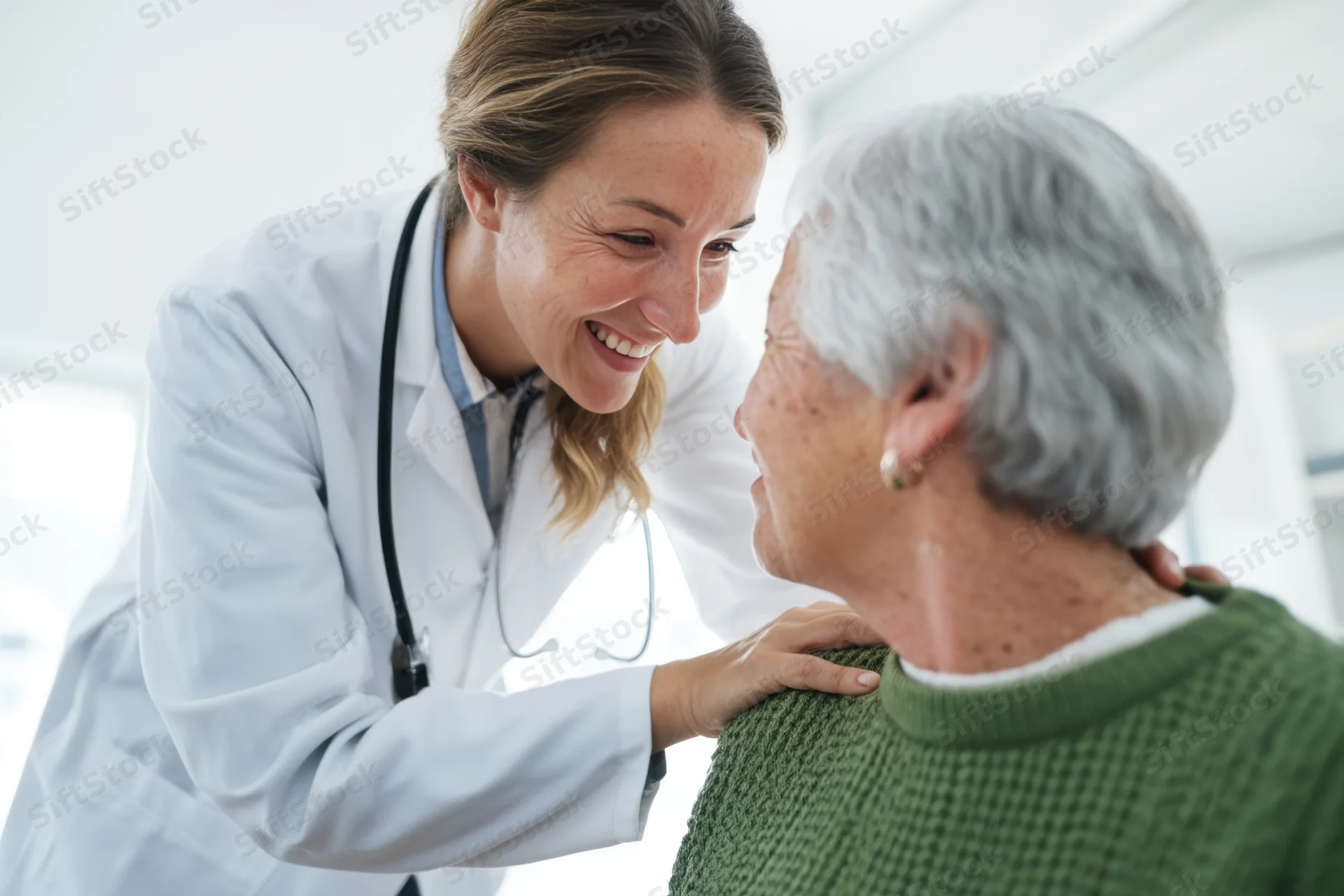 Doctor smiling and placing hands on senior patient's shoulders in clinic