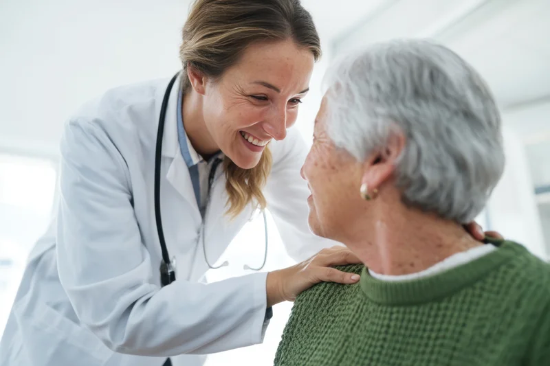 Doctor smiling and placing hands on senior patient's shoulders in clinic