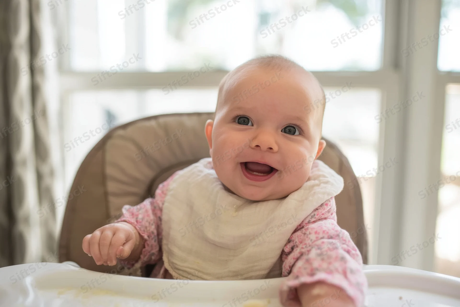 Smiling baby in high chair with bib and crumbs on tray indoors