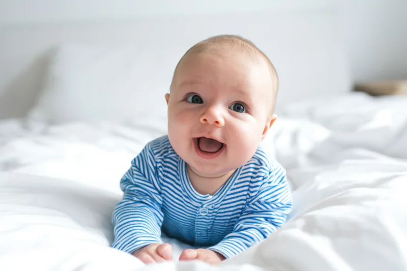 Baby smiling while crawling on white bed in striped blue onesie