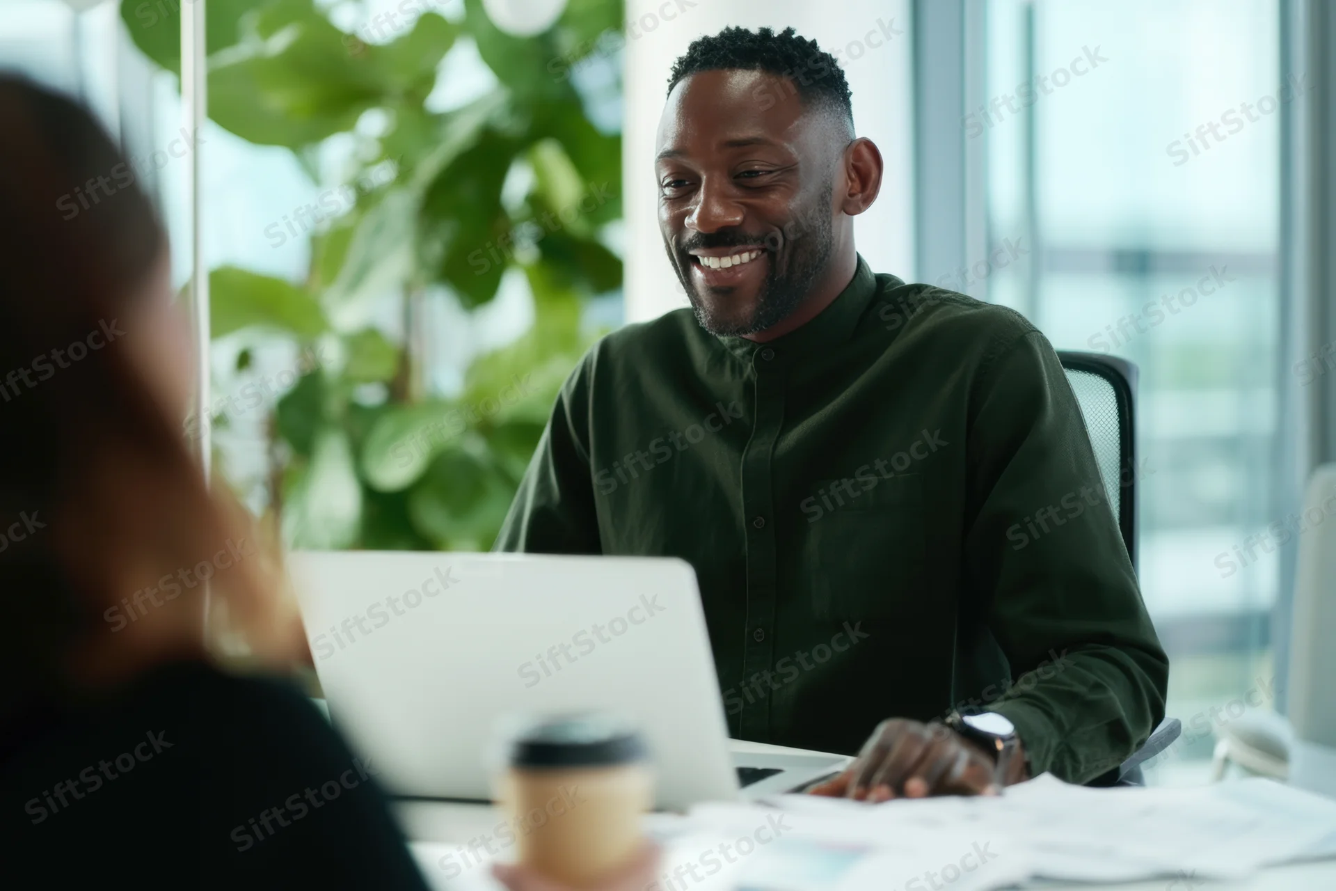 Man smiling during office meeting with woman at desk with laptop and documents