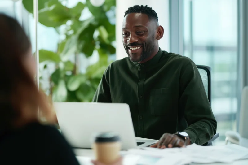 Man smiling during office meeting with woman at desk with laptop and documents