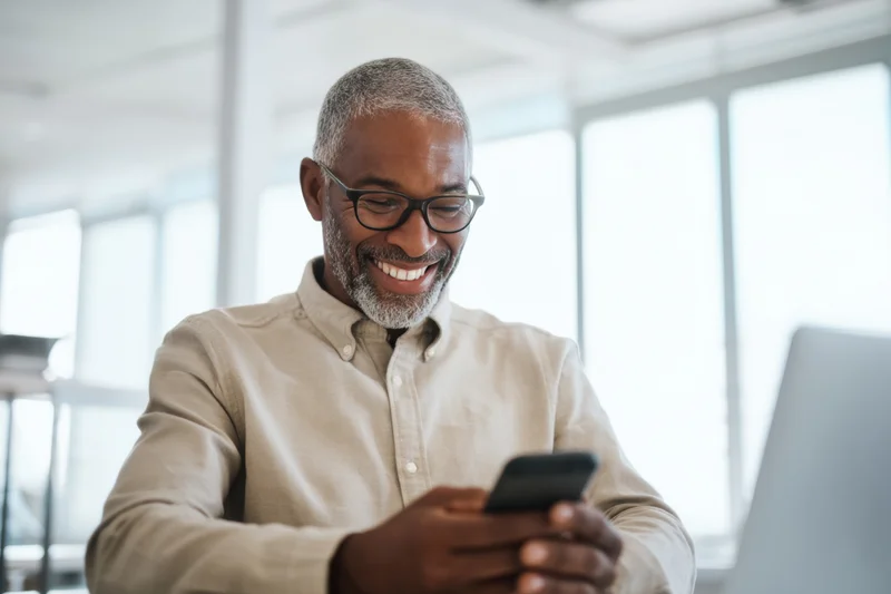 Smiling middle-aged man using smartphone at office desk