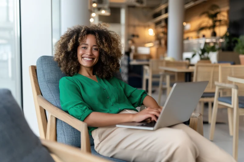 Woman smiling while typing on laptop in modern cafe interior