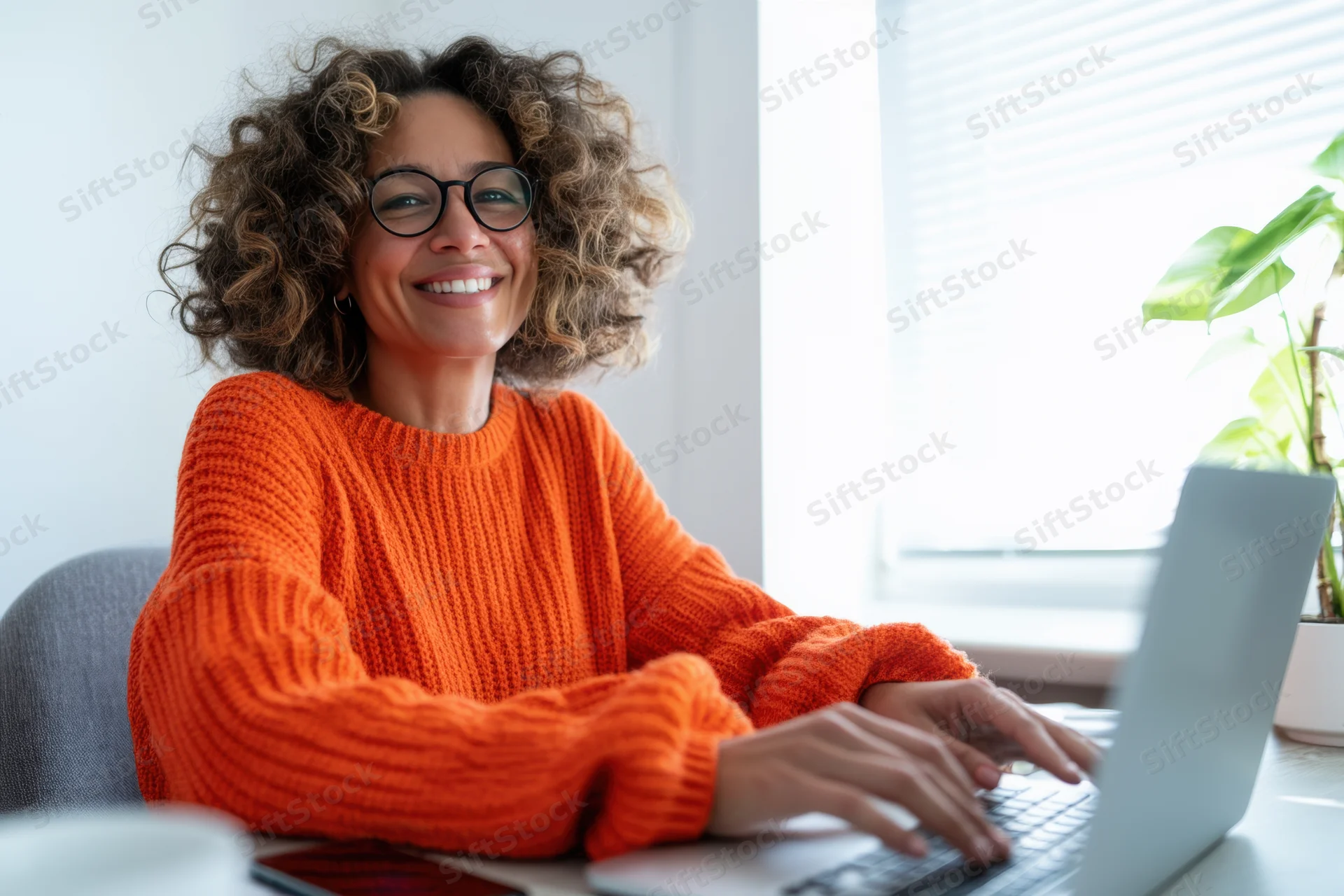 Woman smiling while typing on laptop at home office desk