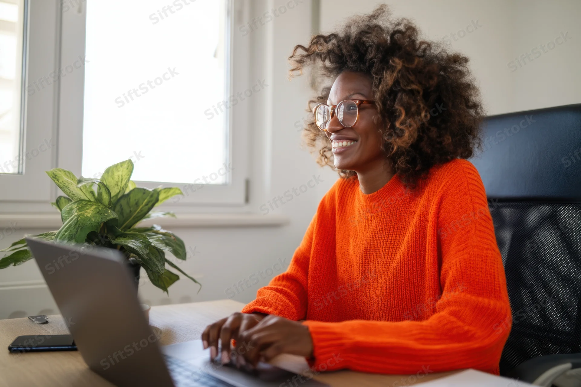 Woman smiling while typing on laptop at desk in home office