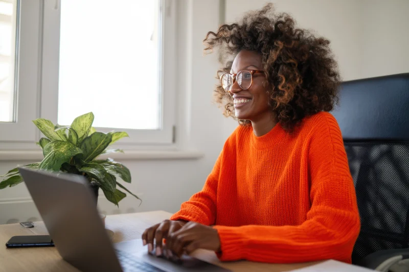 Woman smiling while typing on laptop at desk in home office