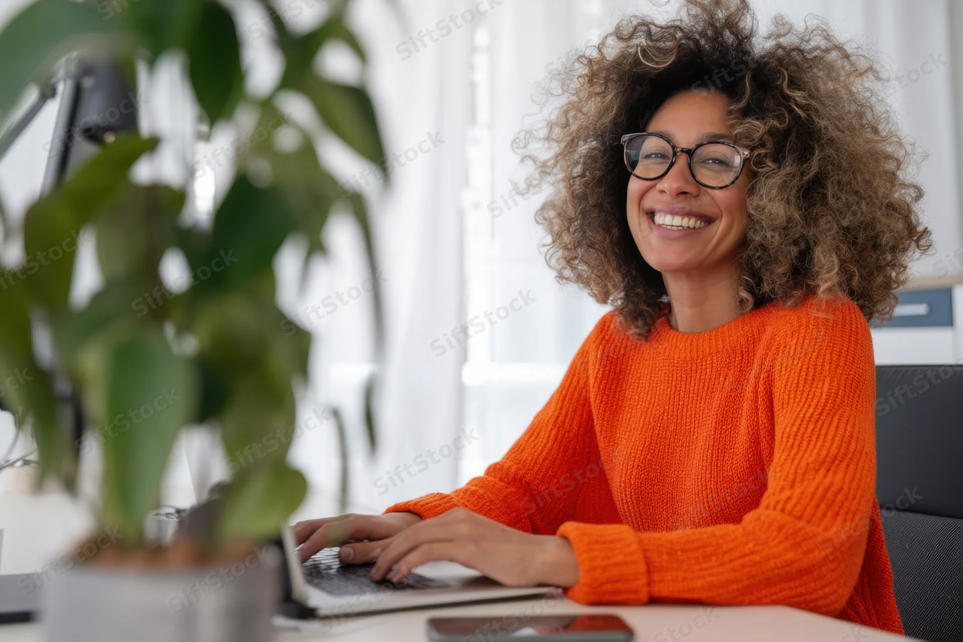 Woman smiling while typing on laptop at home office desk