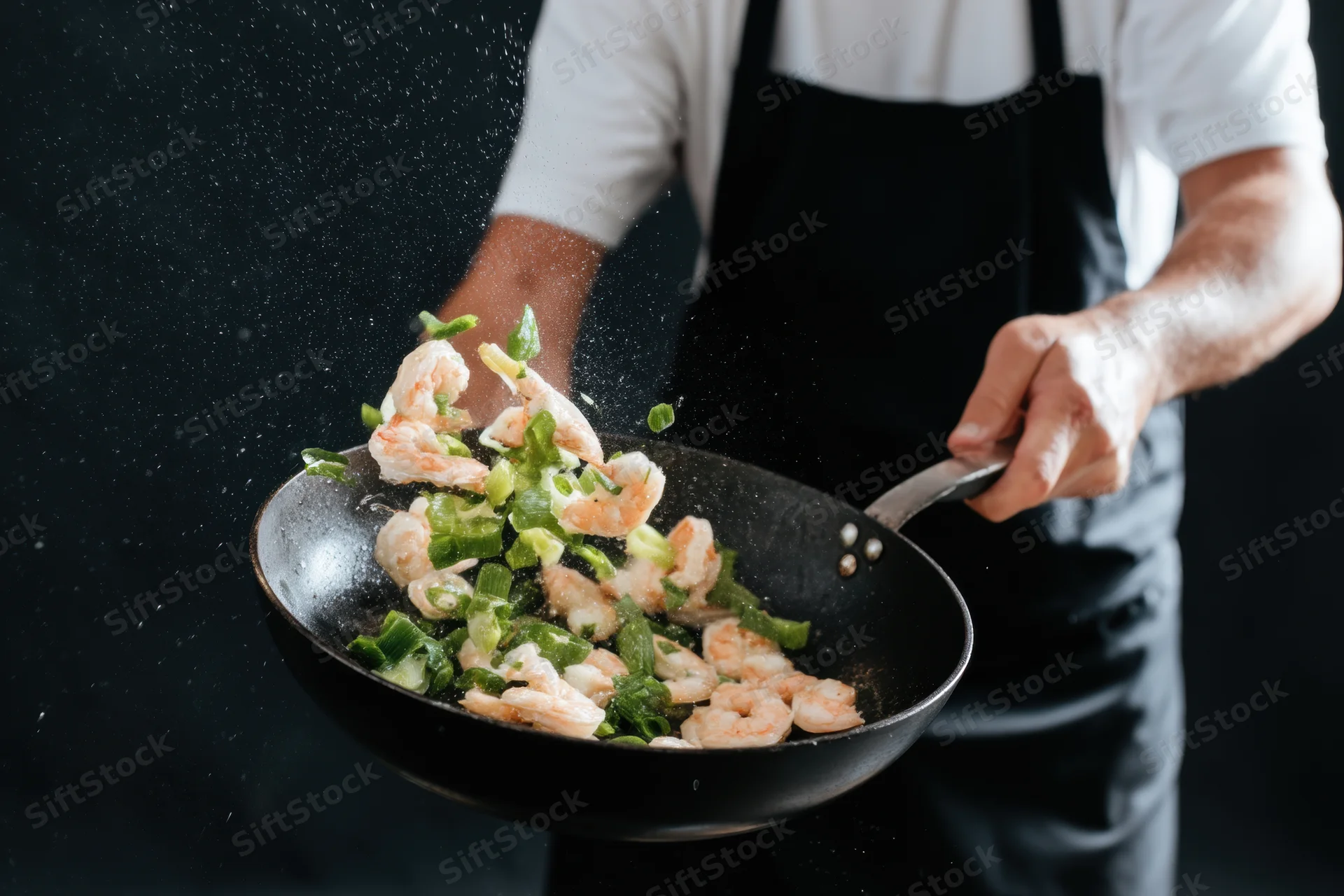 Chef tossing shrimp and green onions in a wok