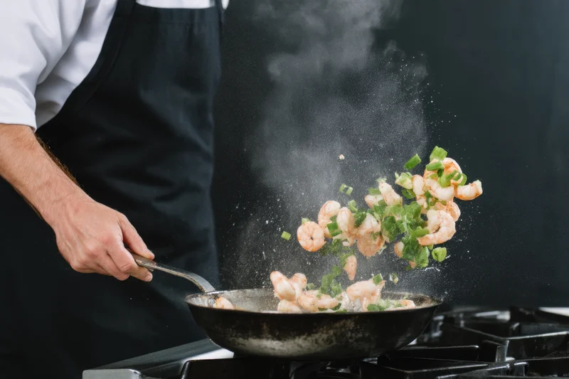 Chef tossing shrimp and green onions in a wok on a stove