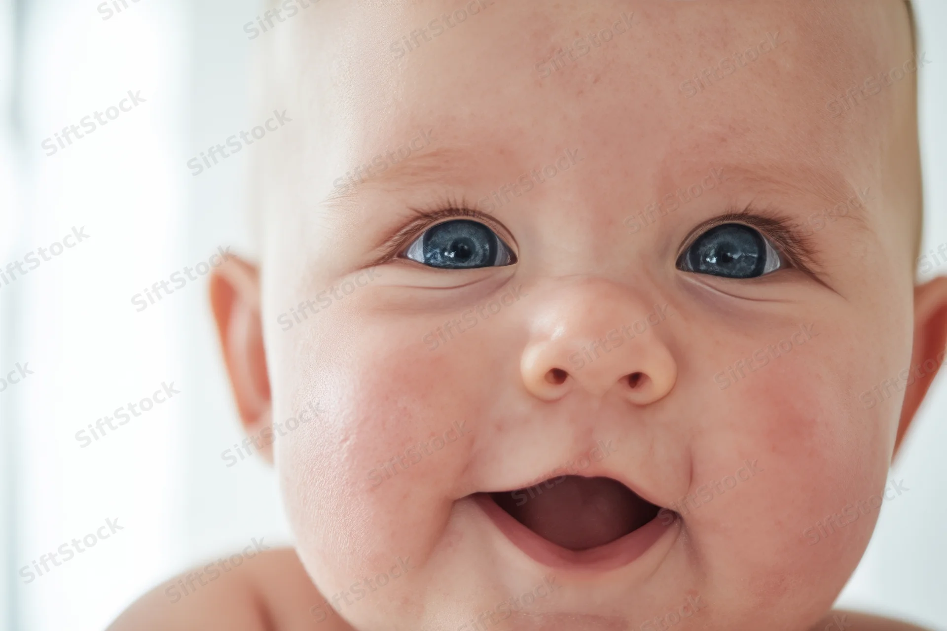 Close-up of a smiling baby with bright blue eyes and rosy cheeks indoors