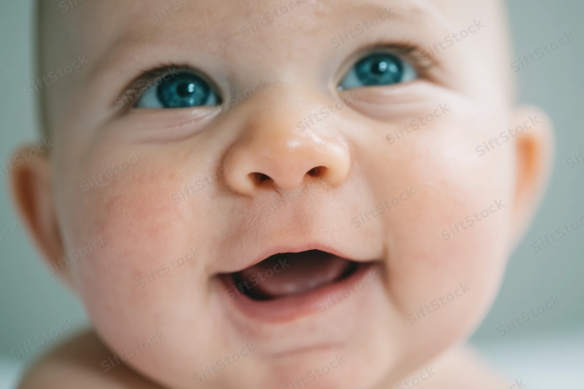 Close-up of a smiling baby with bright blue eyes looking upward