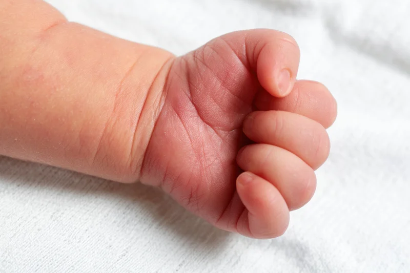 Close-up of a newborn baby's tiny clenched fist resting on a white cloth surface