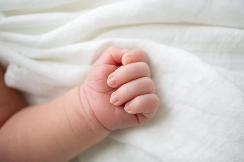 Close-up of a newborn baby's tiny clenched fist resting on a white blanket