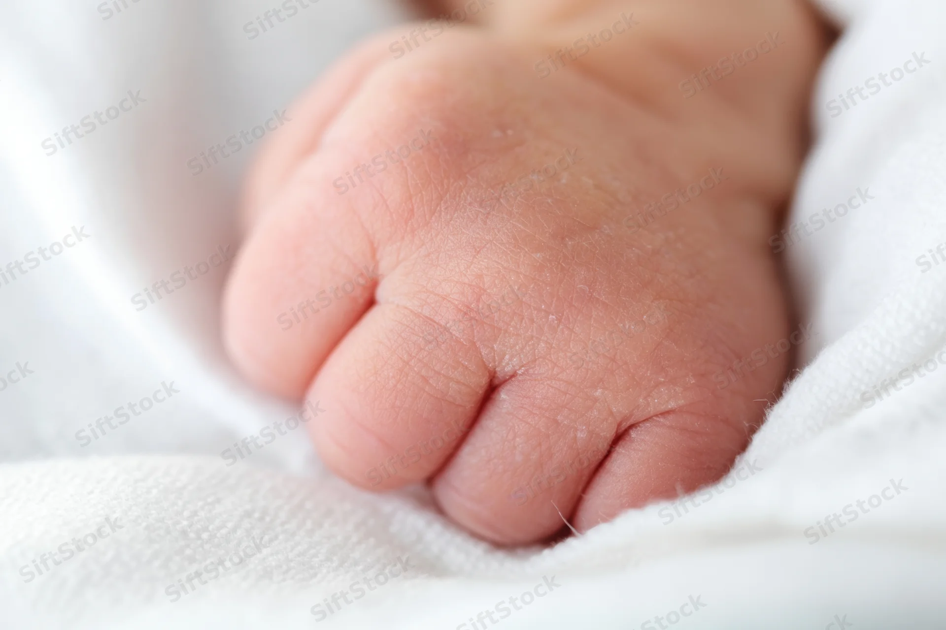 Close-up of a newborn baby's tiny clenched fist resting on a white swaddle blanket