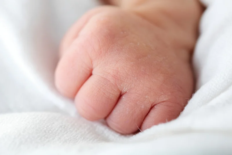 Close-up of a newborn baby's tiny clenched fist resting on a white swaddle blanket