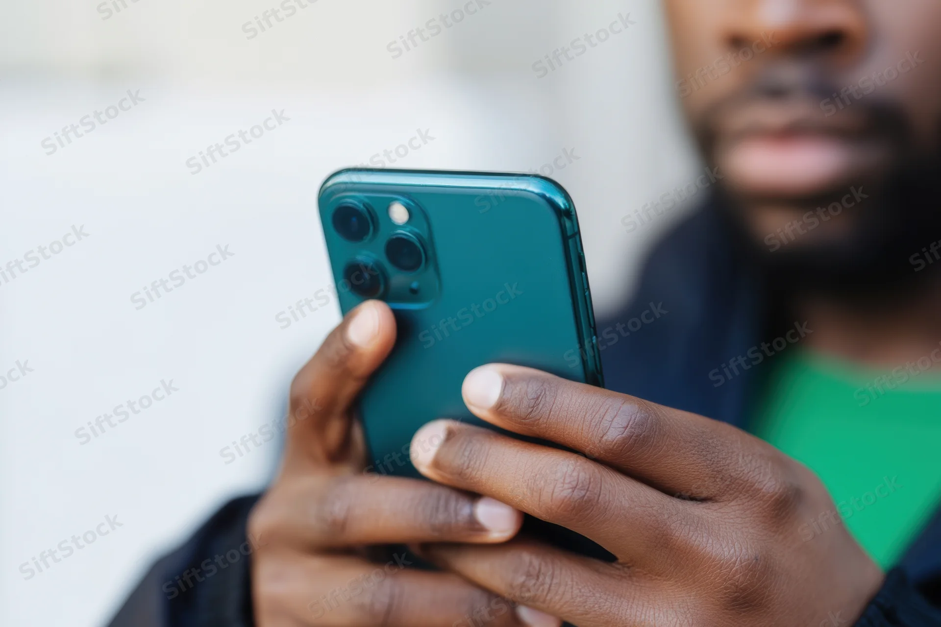 Man holding smartphone with triple camera in green jacket and shirt outdoors