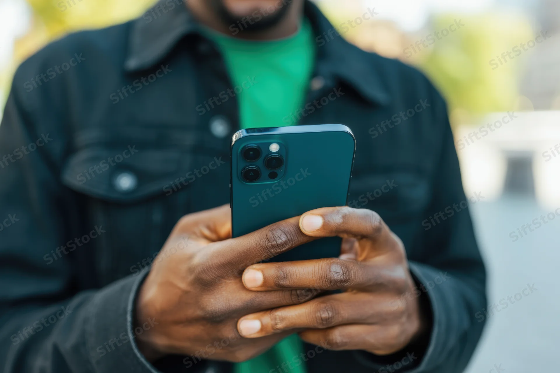 Man holding smartphone outdoors in dark jacket and green shirt
