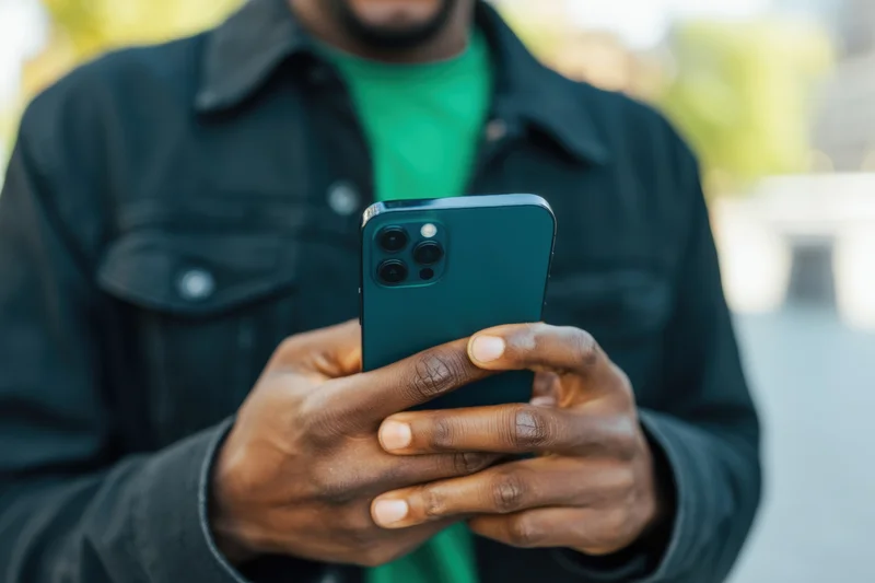 Man holding smartphone outdoors in dark jacket and green shirt