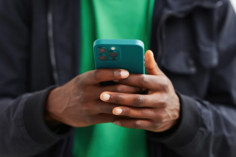 Man holding smartphone with both hands, wearing green shirt and dark jacket