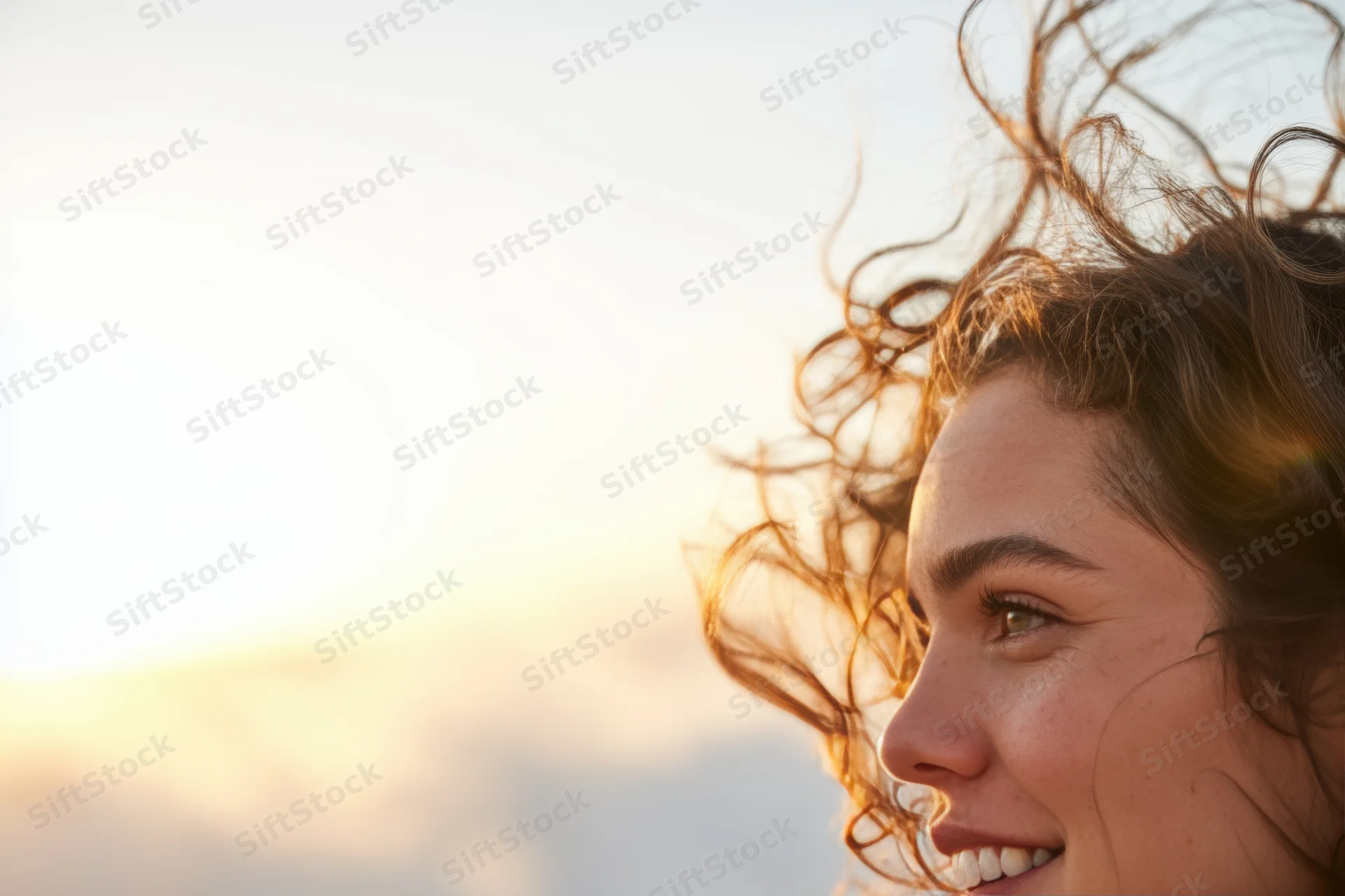 Woman in profile smiling with wind-tossed hair in warm sunlight outdoors