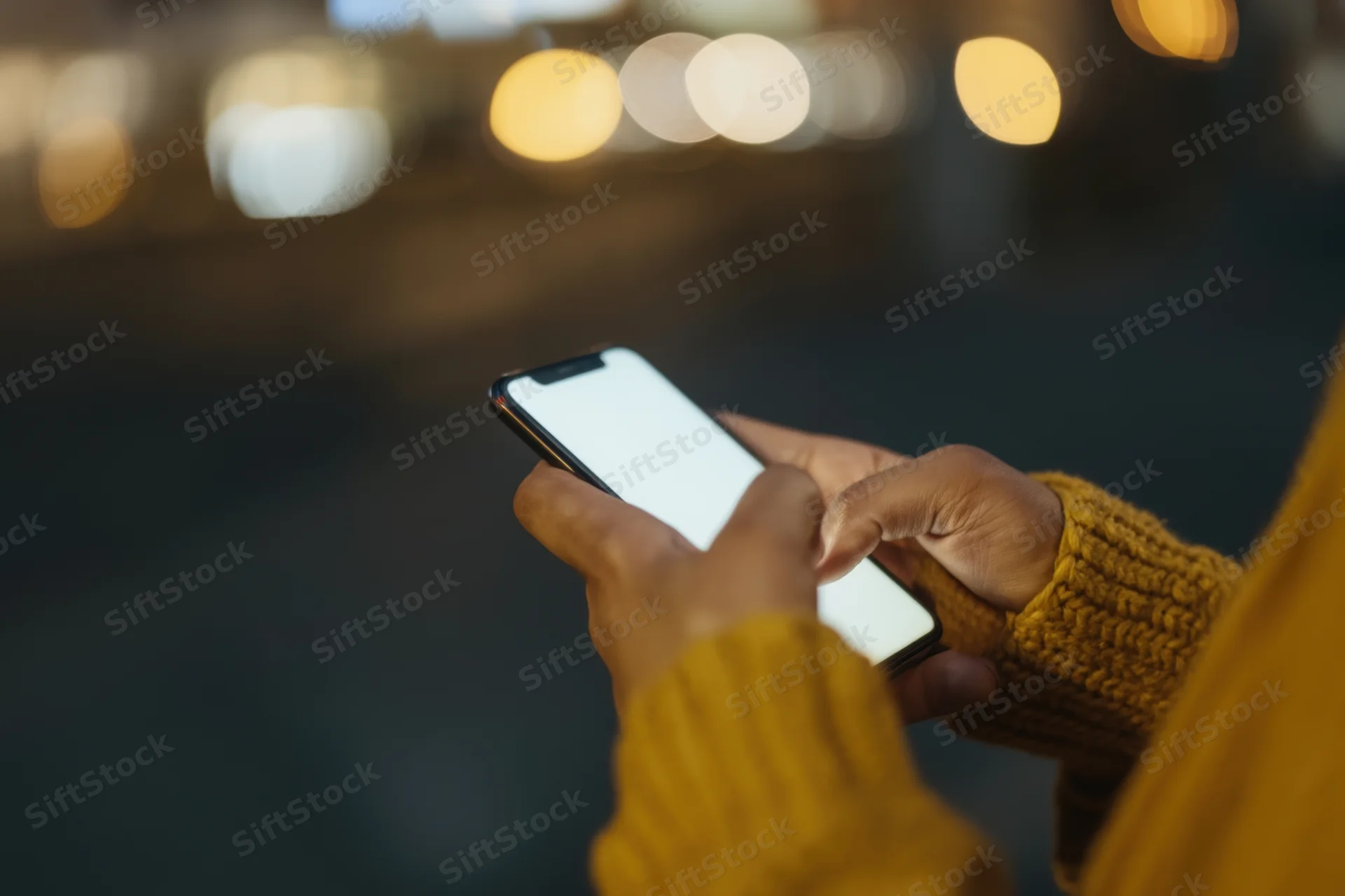 Woman's hands holding smartphone with bright screen in city at night