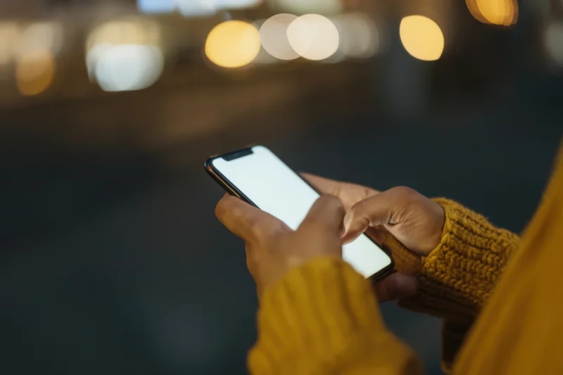 Woman's hands holding smartphone with bright screen in city at night
