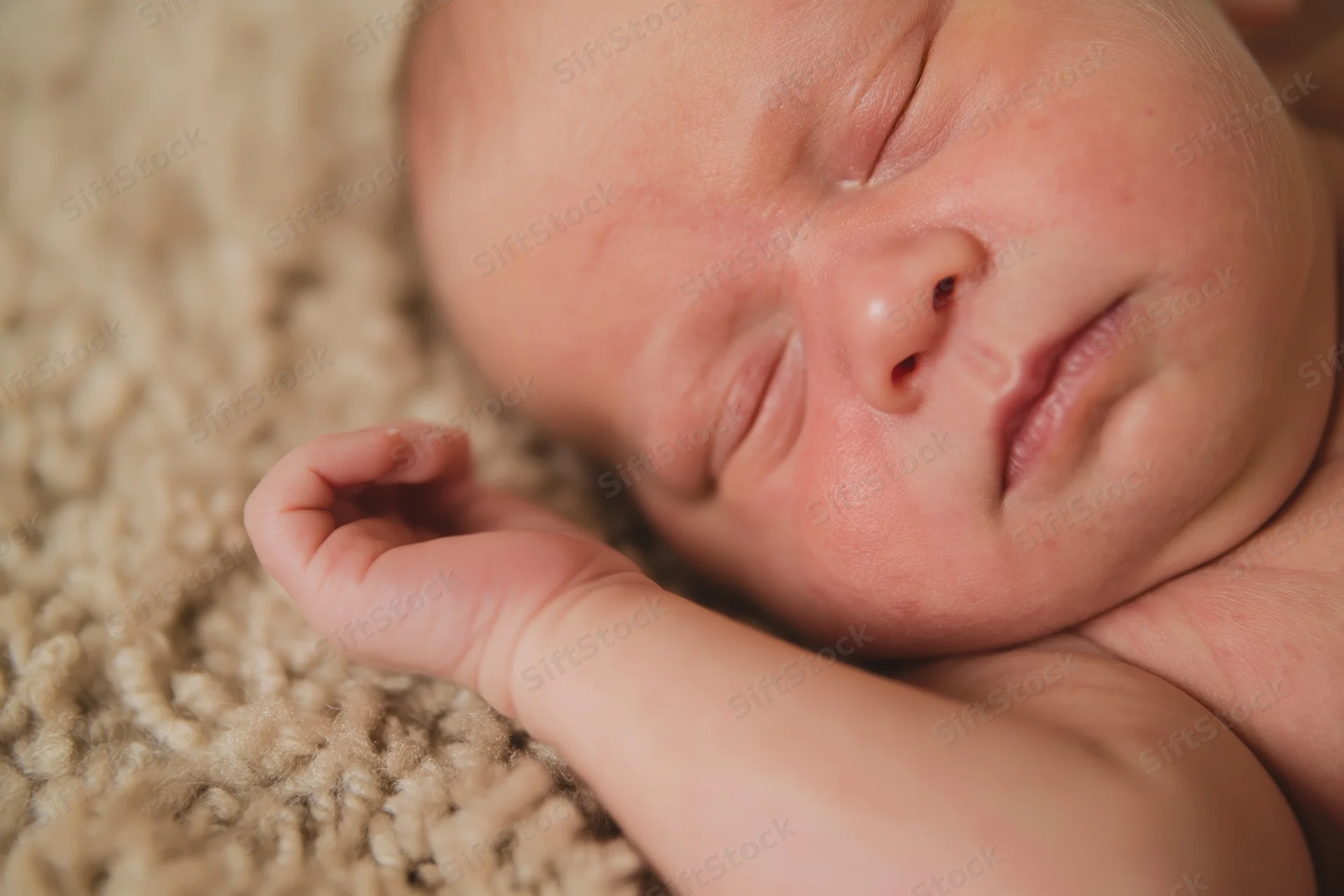 Sleeping newborn baby resting on soft beige carpet with hand curled near face