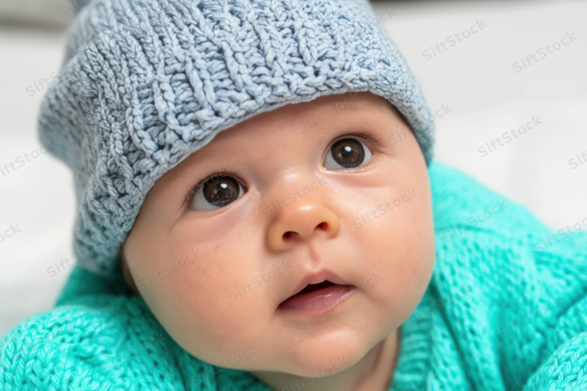 Baby wearing knit hat and sweater looking up indoors