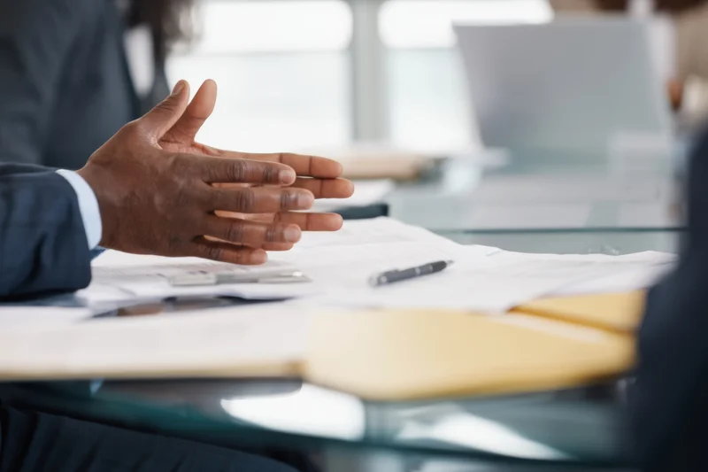 Man gesturing over documents on glass conference table in office meeting