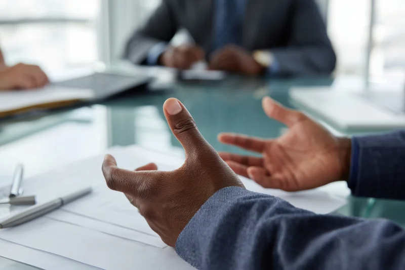 Hands gesturing over documents on a glass conference table in an office meeting