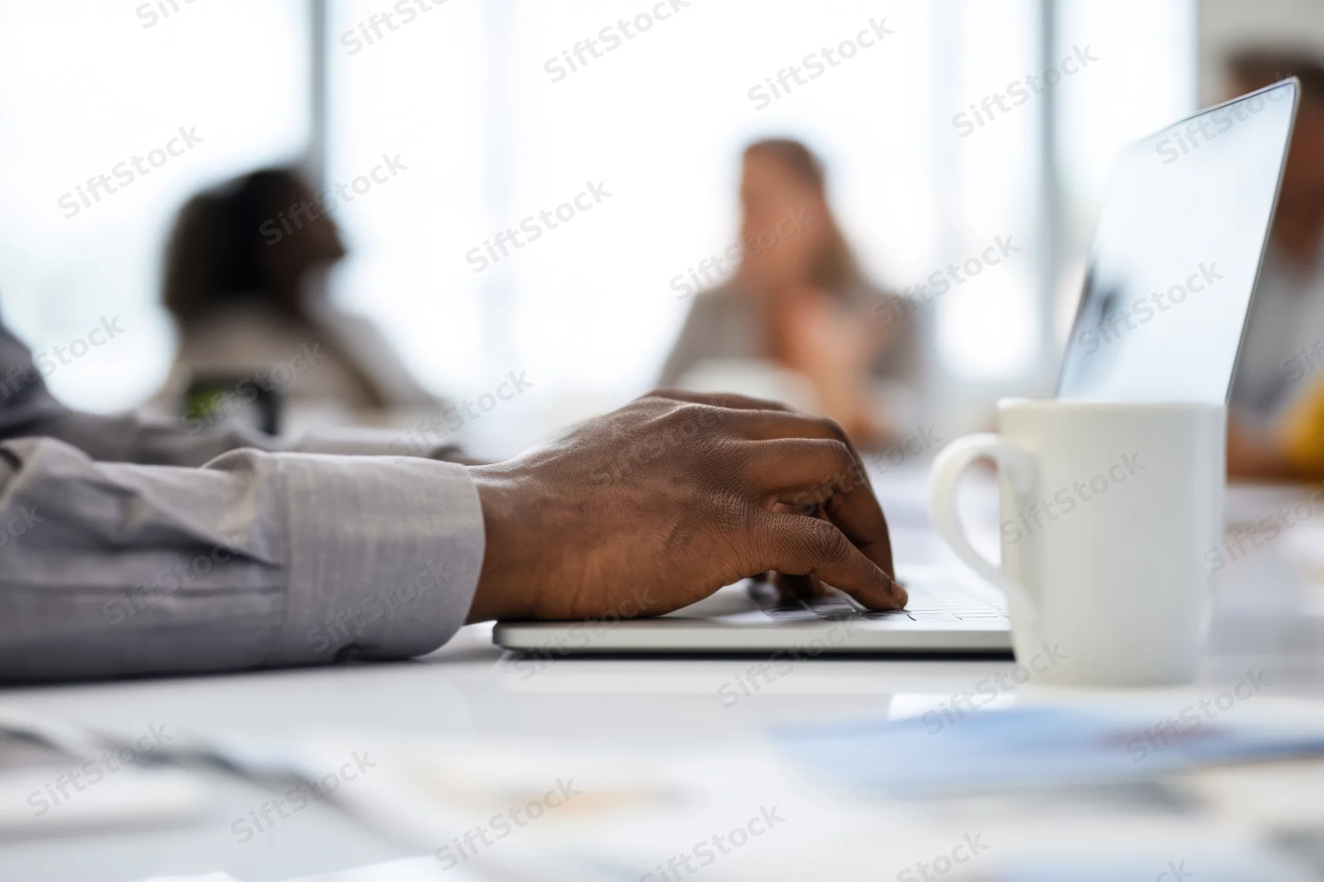 Close-up of hands typing on laptop at conference table with mug and documents