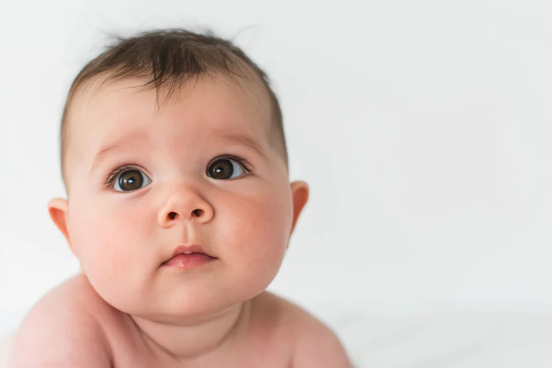 Close-up portrait of a baby with rosy cheeks and soft skin looking up against a white background