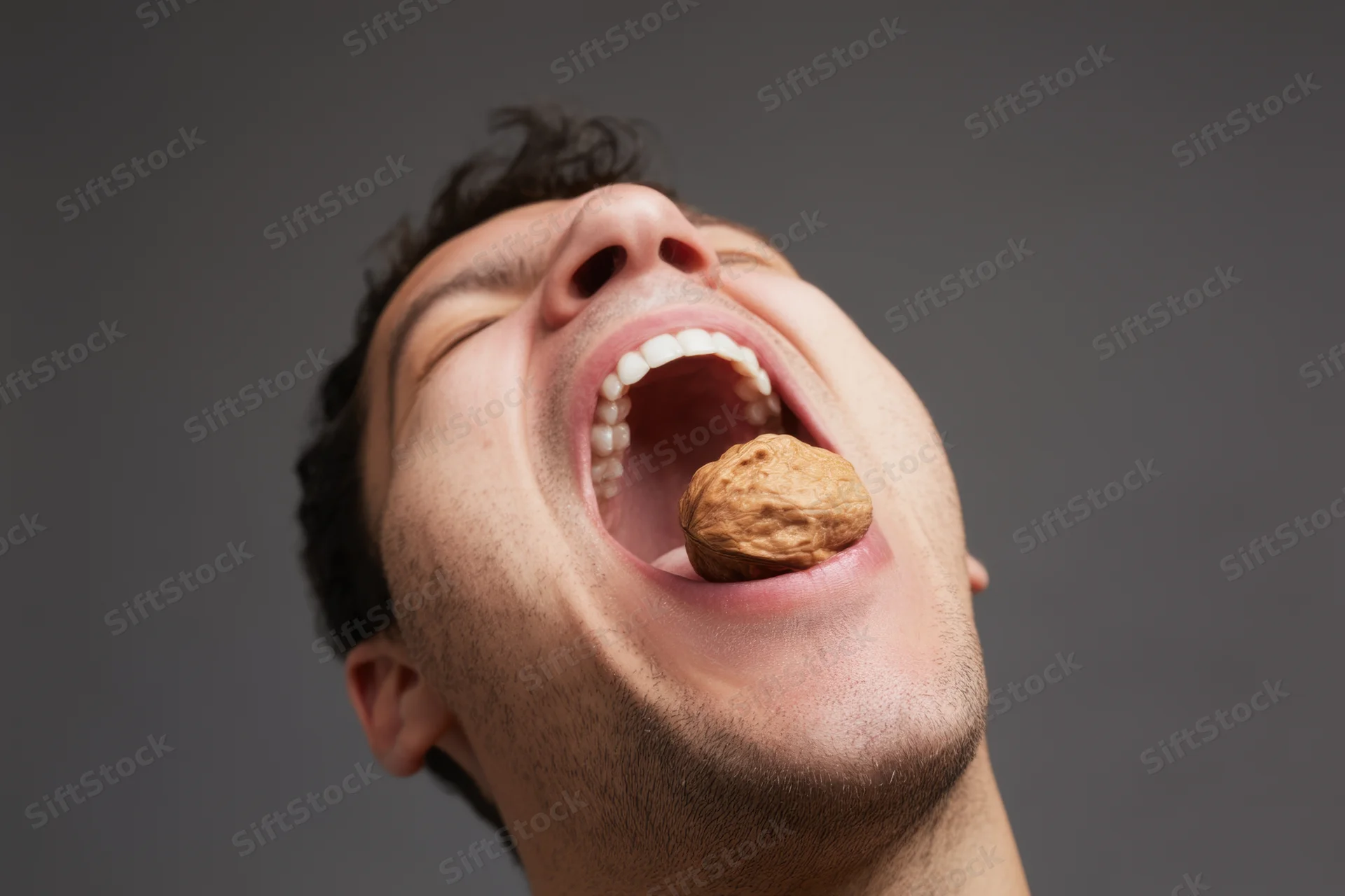 Man with mouth wide open biting into a walnut in studio setting