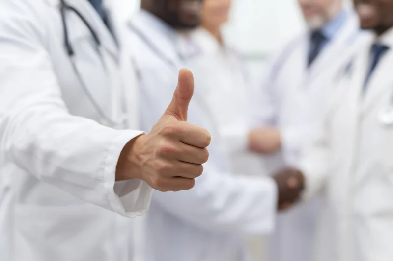 Doctor giving thumbs up with medical team in white coats in hospital setting