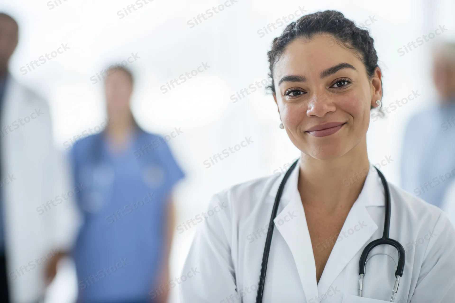 Woman doctor in white coat with stethoscope smiling at camera in clinic setting