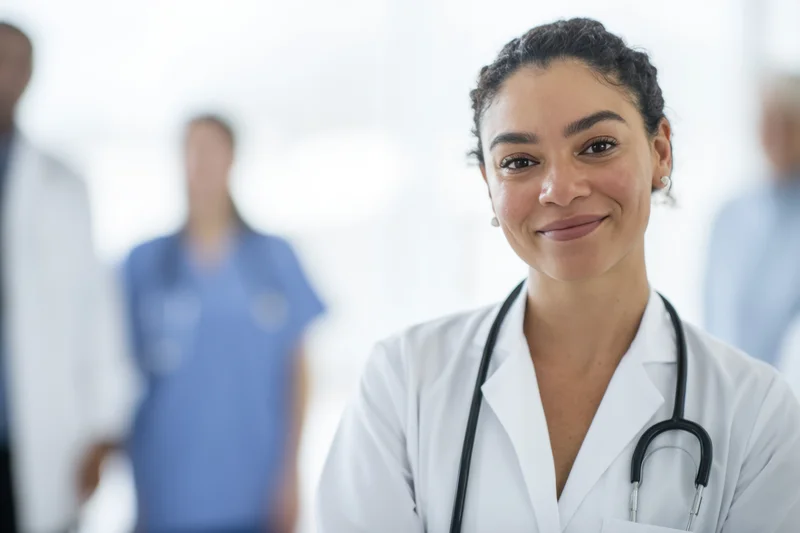 Woman doctor in white coat with stethoscope smiling at camera in clinic setting