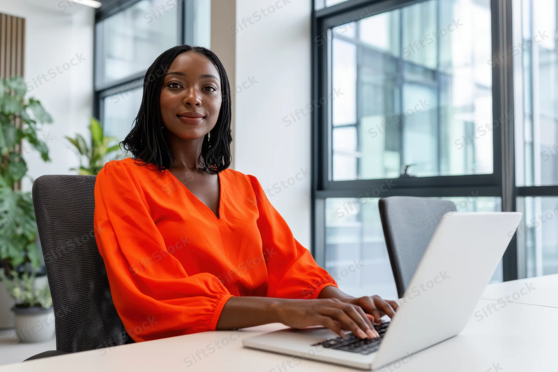 Woman typing on laptop at office desk smiling at camera