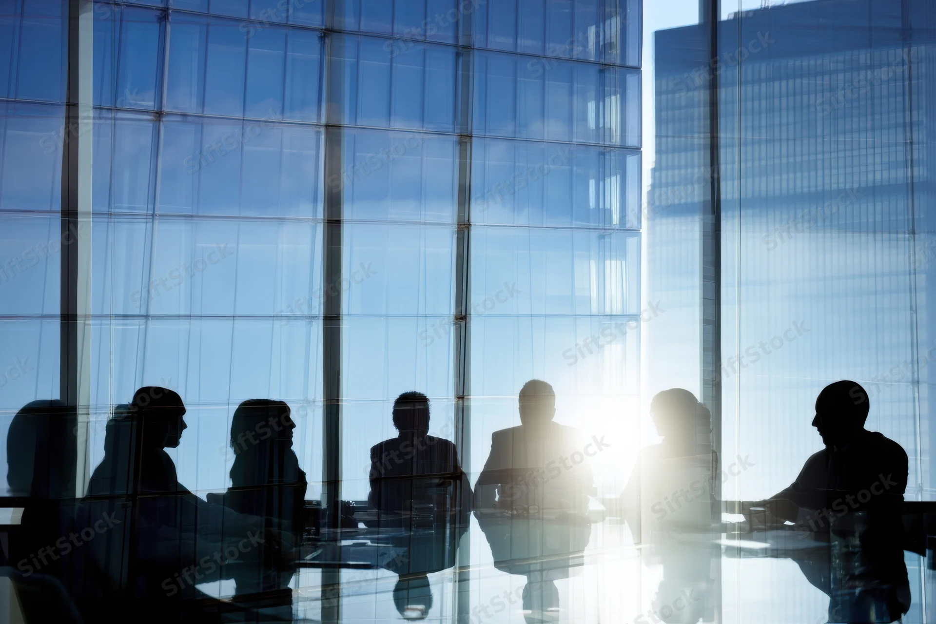 Silhouetted professionals in a corporate meeting at a glass-walled office overlooking a city skyline