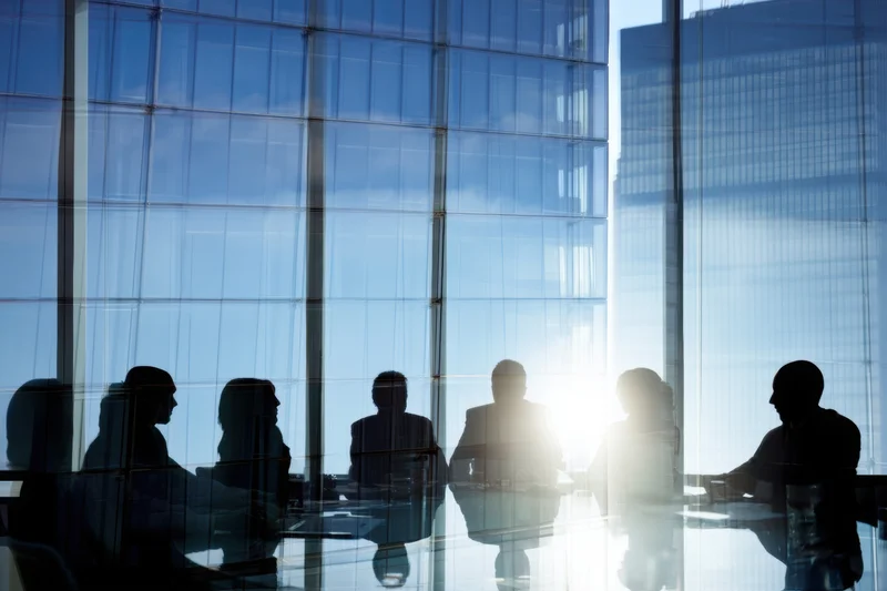 Silhouetted professionals in a corporate meeting at a glass-walled office overlooking a city skyline