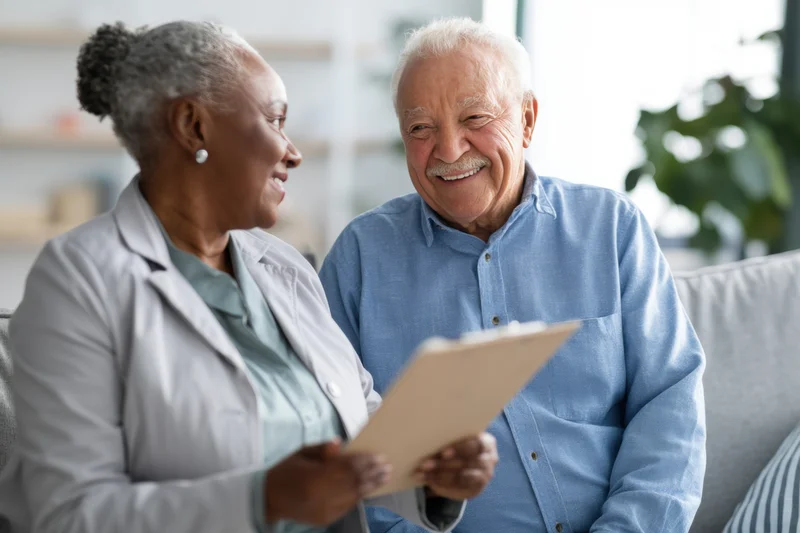 Female clinician consulting with elderly man on clipboard in home setting