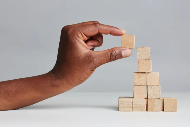Hand placing wooden block atop a growing tower on a white surface