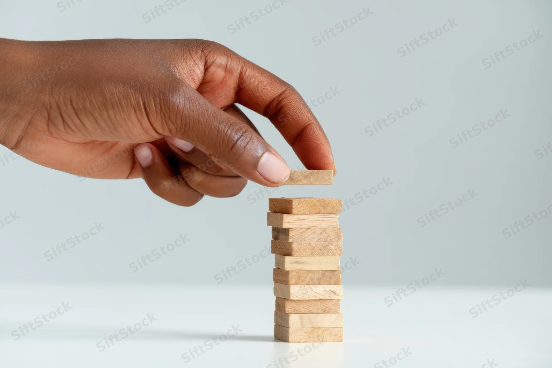 Hand removing top block from wooden tower on white surface