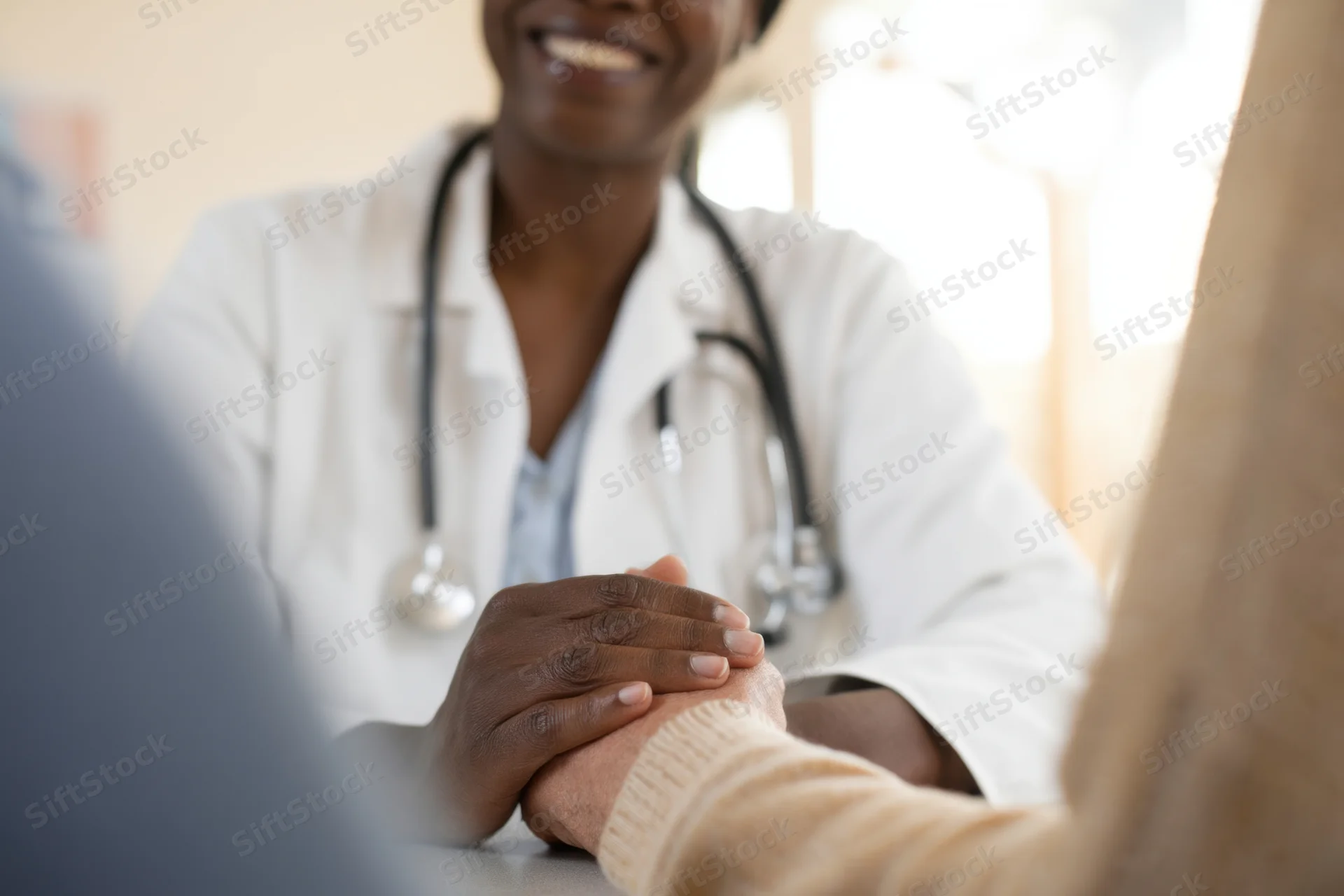 Doctor in white coat holding patient's hand during consultation in clinic