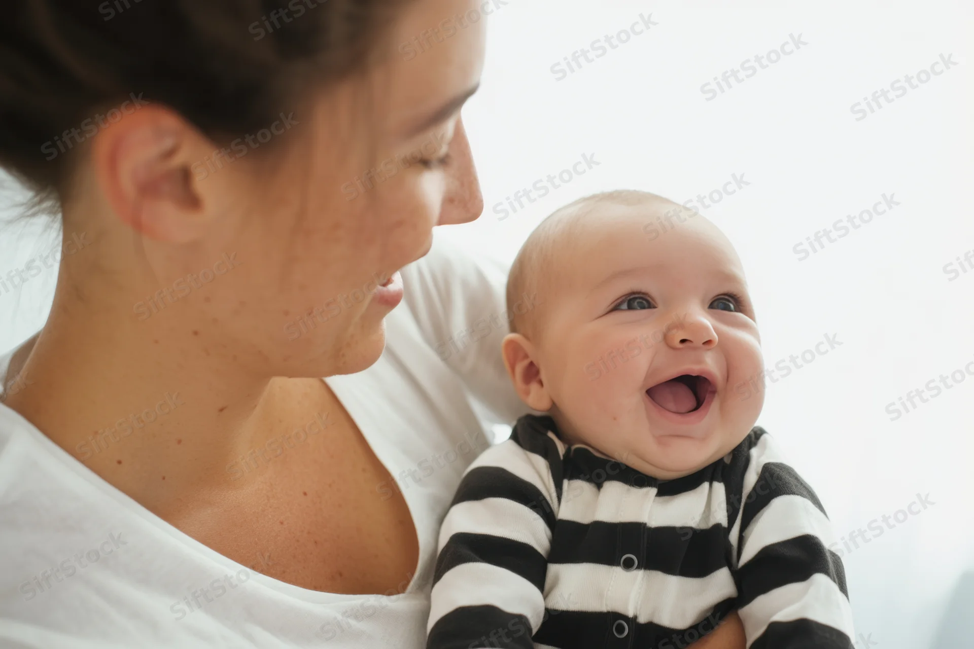 Mother holding smiling baby in striped onesie indoors